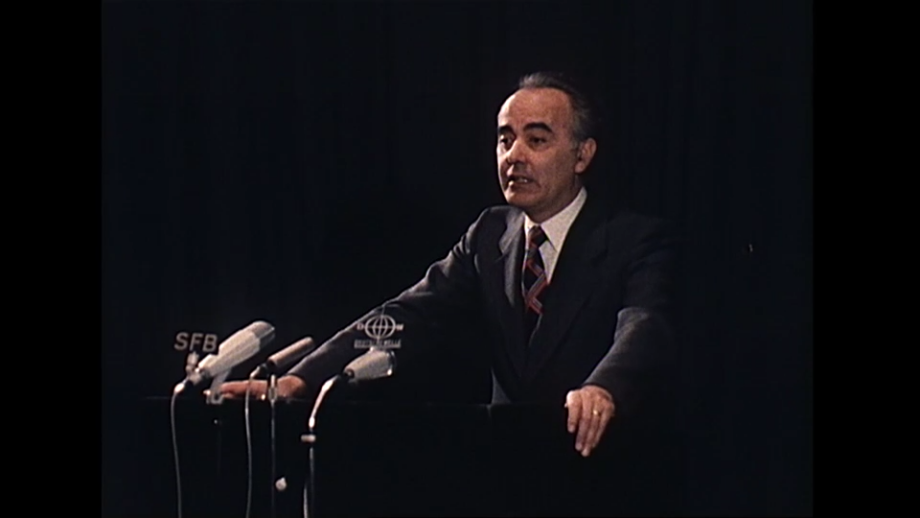 Festrede von Hans Friedrichs (FDP), Bundesminister für Wirtschaft (1972 -1977); Das Bild zeigt Hans Friderichs, einen deutschen Politiker, der als Bundesminister für Wirtschaft von 1972 bis 1977 diente. Er ist auch Jurist und Geschäftsmann. Er hält die Festrede beim Jubiläum zum 50. Jahrestags der Gründung des Deutschen Instituts für Wirtschaftsforschung. Er steht am Podium und spricht in verschiedene Mikrofone. <br />
Visuelle Elemente:<br />
Person: Hans Friedrichs trägt eine Brille und ein Anzug. Er hat graues Haar und einen neutralen Gesichtsausdruck.<br />
Hintergrund: Der Hintergrund ist neutral und unauffällig, was die Aufmerksamkeit auf die Person lenkt.