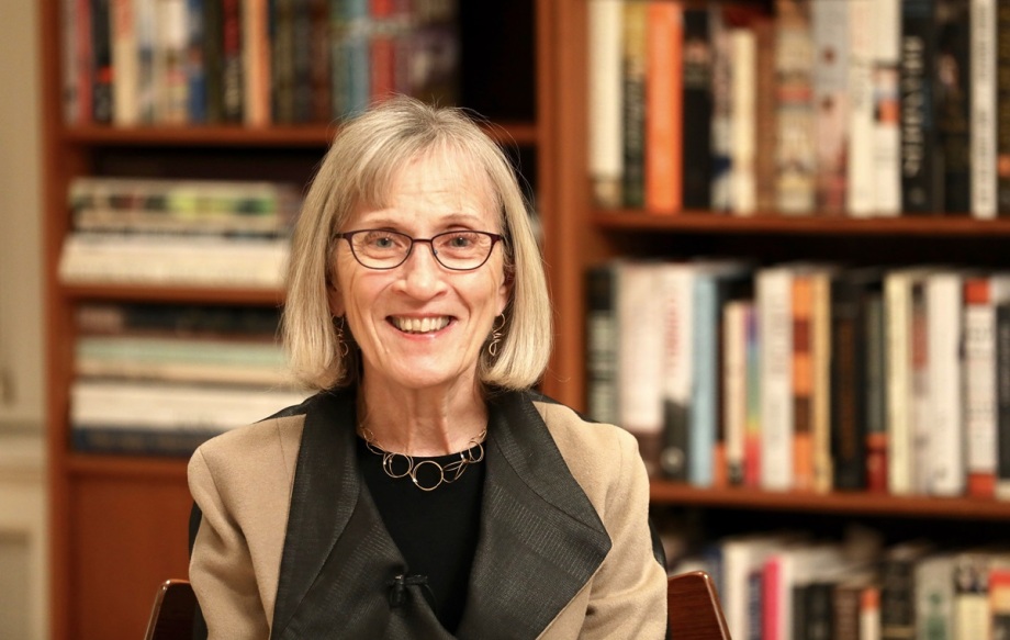 Claudia Goldin erhielt 2023 für ihre Forschung zu geschlechtsspezifischen Unterschieden am Arbeitsmarkt den Wirtschaftsnobelpreis.; Das Bild zeigt die Wirtschaftsnobelpreisträgerin Claudia Golding. Sie nimmt den größten Teil des Bildes ein und ist scharf dargestellt.  Der Hintergrund, bestehend aus einem Bücherregal, ist unscharf und dient als Rahmen für das Porträt. Die Frau ist in einem neutralen, beigen Blazer und einem schwarzen Oberteil gekleidet. Sie wirkt entspannt und freundlich, und lächelt. Die Frau trägt eine Brille und ihr Haar ist grau. Die Bücher im Regal sind unterschiedlich farblich und unklar.<br />
<br />
Das Bild ist ein fotografisches Porträt. Die technische Ausführung ist professionell und zeigt gute Bildqualität, der Fokus ist auf die Frau gerichtet, der Hintergrund ist unscharf. Der Stil ist sachlich und neutral.