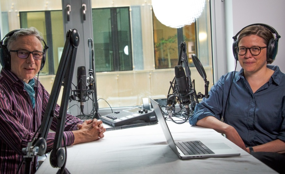 Anna Bindler im Gespräch mit Host Erich Wittenberg.; Das Bild zeigt eine Podcast-Aufnahme in einem modernen Studio. Links im Bild sitzt Erich Wittenberg, der Host des Podcasts, vor einem Mikrofon. Er trägt ein gestreiftes Hemd in Violett- und Blautönen, eine türkisfarbene Krawatte und eine große, dunkle Brille. Rechts ihm gegenüber sitzt Anna Bindler, Leiterin der Abteilung Kriminalität, Arbeit, Ungleichheit. Sie trägt ein dunkelblaues Hemd und ebenfalls eine Brille. Beide Personen tragen Kopfhörer und schauen freundlich in die Kamera.<br />
<br />
Zwischen ihnen befindet sich ein Tisch mit Tonaufnahme-Equipment, zwei professionellen Mikrofonen und einem geöffneten Laptop. Im Hintergrund ist durch das Fenster ein modernes Bürogebäude zu sehen.